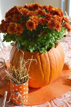 an orange pumpkin sitting on top of a table filled with flowers and other things next to it