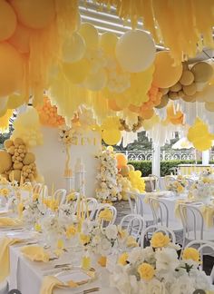 an outdoor event with yellow and white balloons hanging from the ceiling, tables set up for a party