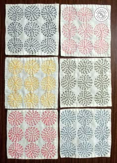 four squares with different designs on them sitting on a wooden table next to each other