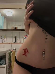 a woman with a tattoo on her stomach holding up the side of her body in front of a mirror