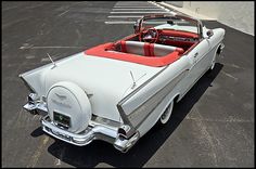 an old white convertible car parked in a parking lot next to a red leather seat