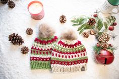 two knitted hats sitting on top of a table next to pine cones and candles