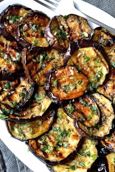 grilled eggplant with brown sauce and parsley in a white serving dish