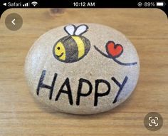 a rock with the words happy painted on it and a bee holding a red heart