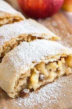 an apple pie is cut in half on a cutting board with powdered sugar around it