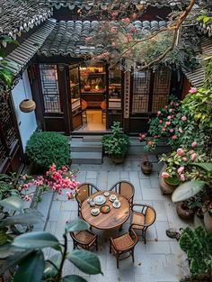 an outdoor dining area with potted plants and flowers on the floor, surrounded by greenery