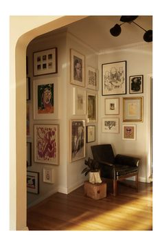 a living room filled with lots of framed pictures on the wall above a black chair