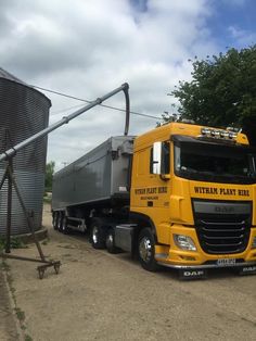 a large yellow truck parked next to a metal silo