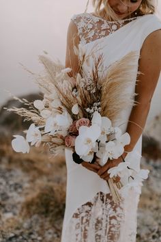 a woman in a white dress holding a bouquet of flowers and grass on top of a hill