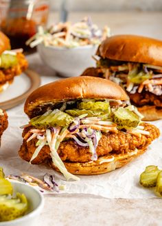 two chicken sandwiches with coleslaw slaw and pickles next to them on paper towels