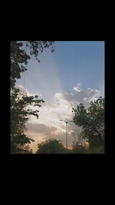 the sun shines brightly through the clouds above trees and street lights in an urban area