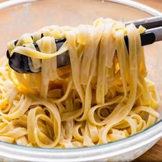 a bowl filled with noodles and cheese being held by a ladle on top of it