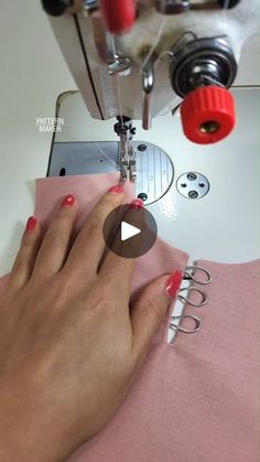 a woman is using a sewing machine to sew on her pink shirt and red nail polish