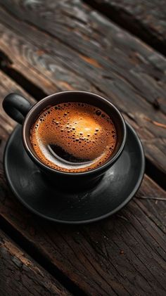 a cup of coffee sitting on top of a black saucer next to a wooden table