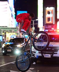 a man on a bicycle is doing tricks in the street at night time with other cars and people