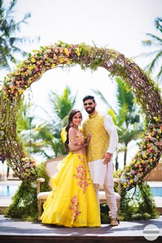 a man and woman standing in front of a circular floral arch with flowers on it