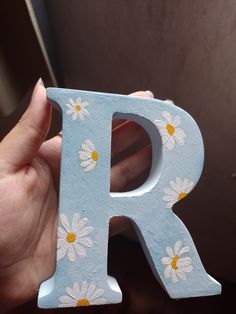 a person holding up a wooden letter with daisies on the letters's sides