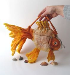 a hand holding a fish made out of fabric and some seashells on a white background