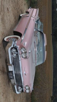 an old pink car is parked in the dirt