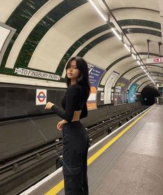 a woman standing in front of a train at a subway station with her hand on her hip