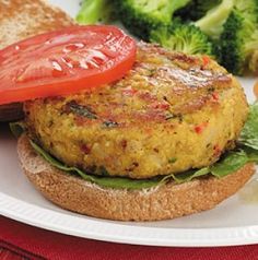 a plate with a burger and some broccoli on the side next to a slice of tomato