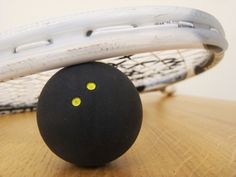 a black ball sitting on top of a wooden table next to a tennis racket