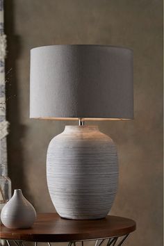 a white vase sitting on top of a wooden table next to a gray lamp shade