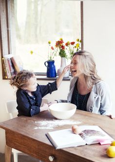 a woman sitting at a table with a child in front of her and an open book