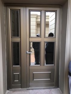 two people are reflected in the windows of a door that has been painted silver and black