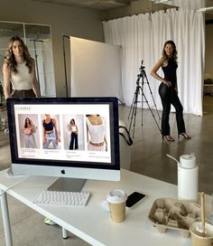 a woman standing behind a computer screen in front of a camera and another person taking pictures