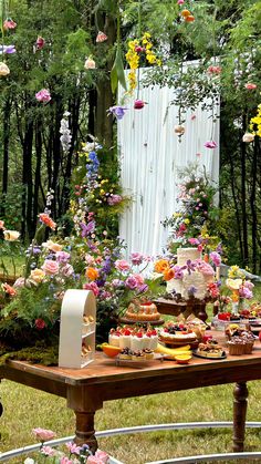 a table with flowers and desserts on it in the middle of a garden area