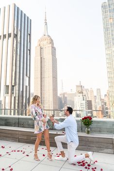 a man kneeling down next to a woman on top of a roof with rose petals