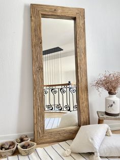 a large mirror sitting on top of a wooden floor next to a white pillow and vase