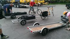 several people are loading and unloading bicycles on trailer trailers in a parking lot with other vehicles