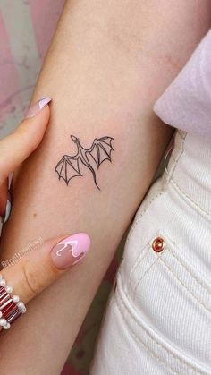 a woman's arm with a small bat tattoo on the left side of her arm