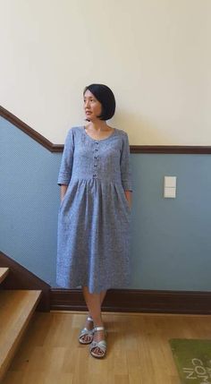 a woman standing in front of some stairs wearing sandals and a dress with buttons on it