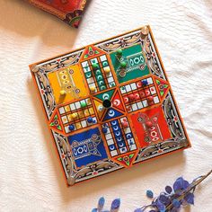 a colorful clock sitting on top of a table next to purple flowers and a book