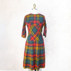 !950's brightly colored wool plaid fit and flare dress in orange, gold, green and black. Fitted at the waist, the bias skirt starts low. It has 3/4 raglan sleeves, a side zipper and 3 covered buttons at the back. There are two breastpockets. It is unlined and has raglan sleeves. Great autumn dress! Fits up to a current size 2 Measurements with room for comfort: Bust up to: 31 inches. Waist up to: 26 inches Hips up to: 37 inches Exact measurements taken flat to compare to a garment which fits wel Fitted Plaid Retro Vintage Dress, Fitted Retro Plaid Vintage Dress, Retro Plaid Fitted Vintage Dress, Fitted Vintage Plaid Dress, Retro Plaid Mini Dress, Fitted Plaid Vintage Dress, Vintage Plaid A-line Dress, Vintage A-line Plaid Dress, Vintage Lined Plaid Dress