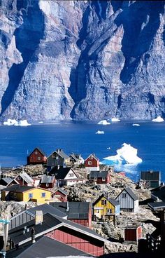 an iceberg floating in the ocean next to some houses and buildings with mountains in the background