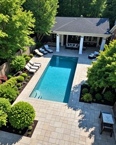 an aerial view of a pool surrounded by trees and shrubs with lounge chairs around it