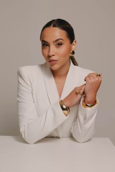 a woman sitting at a table with her hands on her chest and wearing gold bracelets