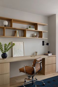 a chair and desk in a room with wooden shelves on the wall above it, along with a blue rug