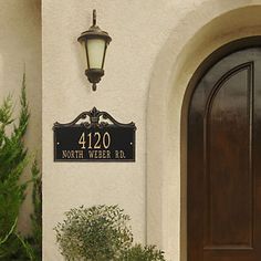 a house number sign mounted to the side of a white building with a potted plant next to it