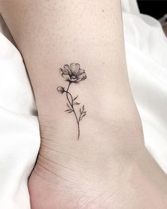 a small flower tattoo on the ankle is shown in black and grey ink, with one single flower at the top