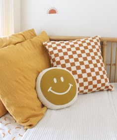 a smiley face pillow sitting on top of a bed next to two yellow and white pillows