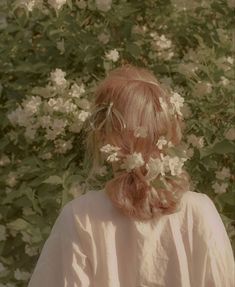 the back of a woman's head with white flowers in her hair and behind her is a bush