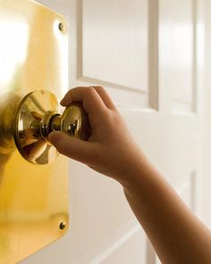 a person's hand is holding the door knob to a gold colored door handle