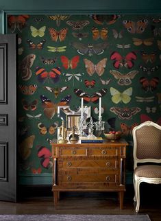 a room with a dresser, chair and wallpaper covered in colorful moths on it