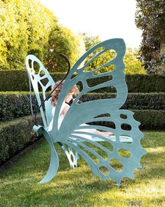 a woman laying on top of a butterfly shaped bench in the grass next to a hedge