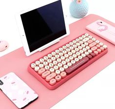 a pink computer keyboard sitting on top of a desk next to a phone and tablet